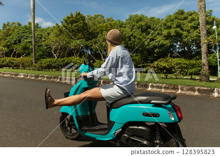 Young woman enjoys a ride on a scooter in a park Young woman enjoys a ride on a scooter in a park 128395823