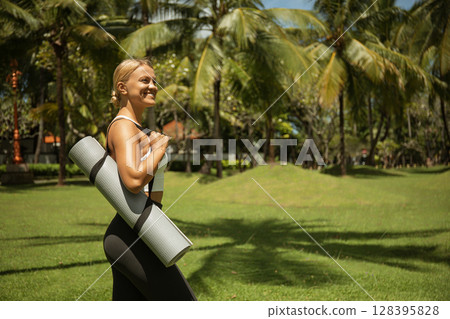 Woman enjoys a sunny day while carrying a yoga mat in the park Woman enjoys a sunny day while carrying a yoga mat in the park 128395828