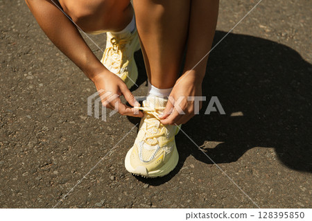 Individual adjusts shoelaces on vibrant sneakers outdoors 128395850