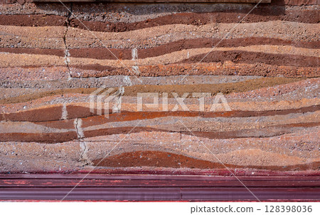 Full frame shot of an earthen wall texture of clay house structure. These walls are constructed by ramming a mixture of aggregates, including gravel, sand, silt and a small amount of clay. Full frame shot of an earthen wall texture of clay house structure. These walls are constructed by ramming a mixture of aggregates, including gravel, sand, silt and a small amount of clay. 128398036