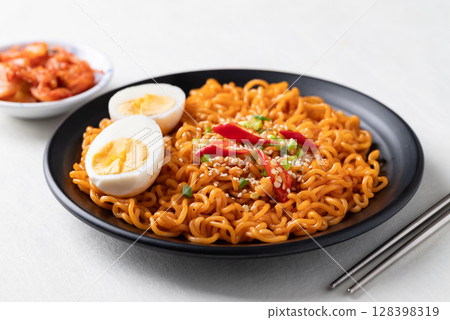 Spicy korean dried instant noodles with boiled egg, scallion, sesame seed, chili and kimchi Spicy korean dried instant noodles with boiled egg, scallion, sesame seed, chili and kimchi 128398319