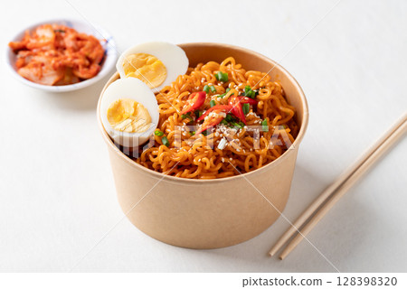 Spicy Korean dried instant noodles with boiled egg, scallion, sesame seed and chili in paper bowl 128398320