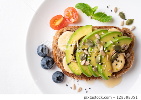 Avocado toast with banana, sunflower seeds, pumpkin seeds, sesame seeds, blueberry, tomato and honey 128398351