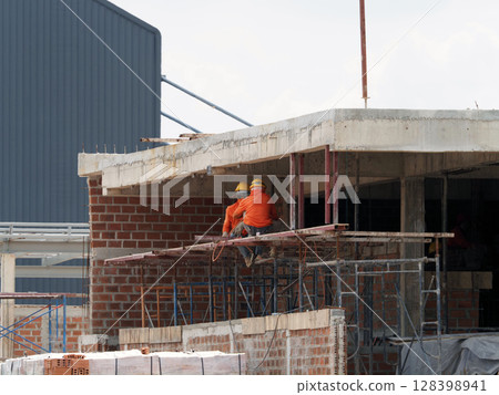 Construction workers wearing safety helmets working on building under construction, with scaffolding and concrete structure visible, in industrial setting 128398941