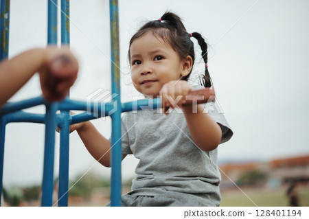 cheerful toddler girl playing on double swing with freind at outdoor playground 128401194