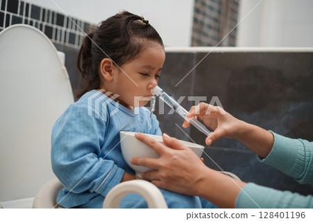 mother making nasal wash for toddler girl with syringe and saline. cleaning nose 128401196