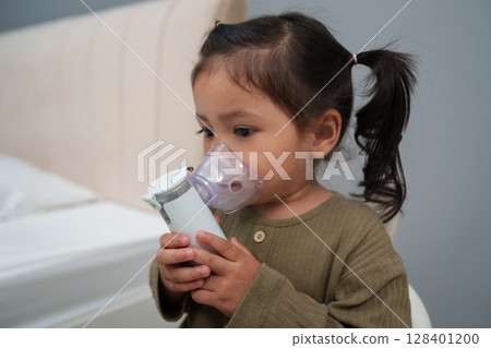 toddler girl making inhalation treatment with nebulizer at home 128401200
