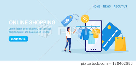 Young woman shopping online using smartphone. Customer choosing modern apparel, wearing, accessories for wardrobe. Clothes hanging on railing hangers with tags. Sale. Internet garment shop 128402893