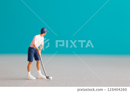 Miniature figurine of a golfer preparing to swing on a vibrant blue background. 128404260