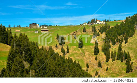 Scenic view of green hills and wooden cabins under a clear blue sky in a mountainous area during daytime Scenic view of green hills and wooden cabins under a clear blue sky in a mountainous area during daytime 128404821