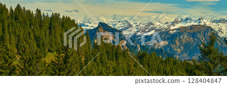 Mountain landscape showcasing verdant pine forests and snow-capped peaks under a bright sky in the Swiss Alps during early spring Mountain landscape showcasing verdant pine forests and snow-capped peaks under a bright sky in the Swiss Alps during early spring 128404847