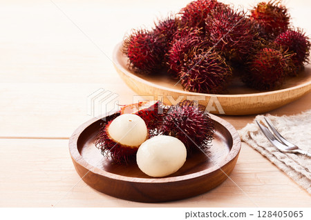 Close-up of rambutan fruit and its peeled white juicy flesh on a wooden plate 128405065