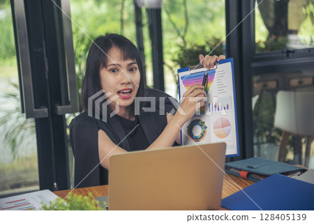 Asian businesswoman vdo call conference telecommunicate office desk. Women show Graph business report online meeting. Freelance women using laptop home office technology. Businesswoman online meeting Asian businesswoman vdo call conference telecommunicate office desk. Women show Graph business report online meeting. Freelance women using laptop home office technology. Businesswoman online meeting 128405139