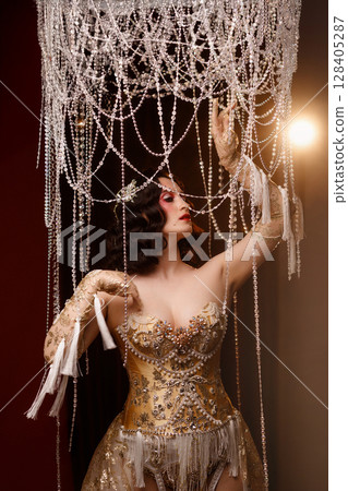 Circus show performer in vintage corset costume under chandelier on dark background 128405287