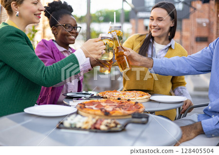 Friends gather outdoors, toasting with drinks and enjoying pizza. A moment of celebration and togetherness captured with smiles and cheer. Friends gather outdoors, toasting with drinks and enjoying pizza. A moment of celebration and togetherness captured with smiles and cheer. 128405504