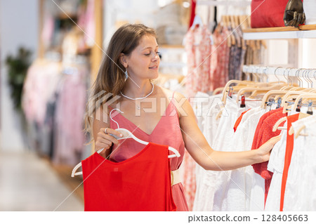 Young woman standing in store and choosing clothes Young woman standing in store and choosing clothes 128405663