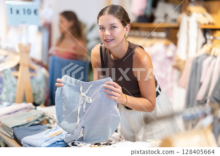 Young woman chooses trousers in clothing store Young woman chooses trousers in clothing store 128405664