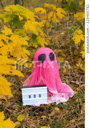 Halloween holiday concept. Handmade pink ghost with Lightbox BOO text made from bandages and glue in autumn forest background. Children's art project. DIY 128405781