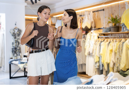 Two female shoppers carefully choosing clothes - dress, jeans, skirts and other clothes in clothing store Two female shoppers carefully choosing clothes - dress, jeans, skirts and other clothes in clothing store 128405905