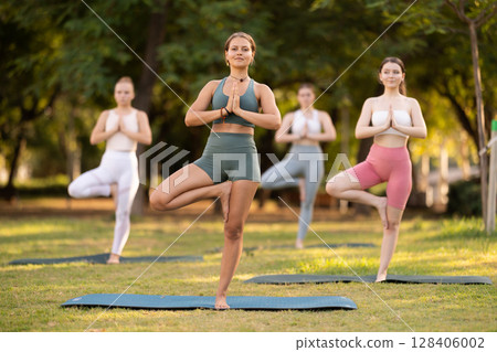 Yoga lesson visitors girls perform vrikshasana in park 128406002
