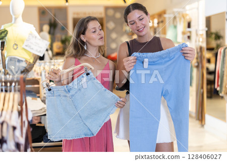 Two young women choosing shorts and trousers in store 128406027