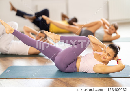 Group of multinational people doing exercises for press during group class in fitness studio Group of multinational people doing exercises for press during group class in fitness studio 128406082