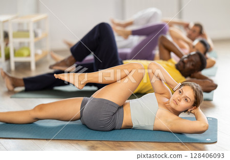 Group of multinational people doing exercises for press during group class in fitness studio Group of multinational people doing exercises for press during group class in fitness studio 128406093