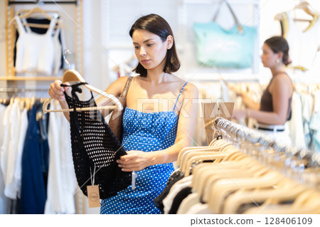 Two young women choosing a dress and other clothes in clothing store Two young women choosing a dress and other clothes in clothing store 128406109