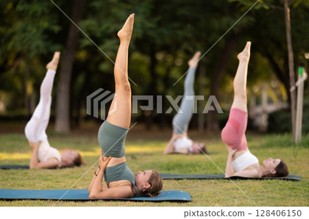 Yoga lesson visitors girls perform Salamba Sarvangasana in park Yoga lesson visitors girls perform Salamba Sarvangasana in park 128406150