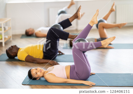 Asian woman doing toe taps exercise with ball at group pilates class Asian woman doing toe taps exercise with ball at group pilates class 128406151