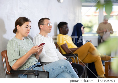 Young woman waiting in line with phone in her hand 128406204