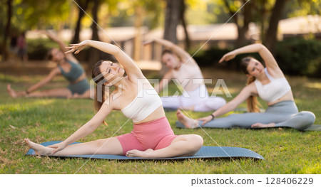 Yoga lesson visitors girls perform Parivritta Janu Shirshasana in park 128406229