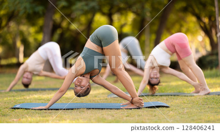 Yoga lesson visitors girls perform Adho Mukha Svanasana in park 128406241