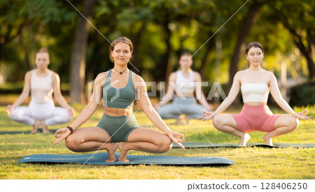Yoga training in summer sunny park - girls in kagasana pose on mats 128406250