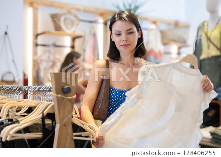 Two female shoppers carefully choosing clothes - dress, jeans, skirts and other clothes in clothing store Two female shoppers carefully choosing clothes - dress, jeans, skirts and other clothes in clothing store 128406255