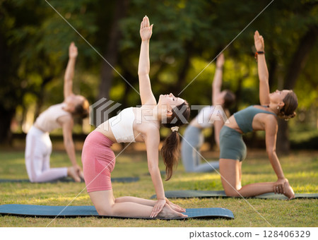 Yoga lesson visitors girls perform Ushtrasana in park 128406329