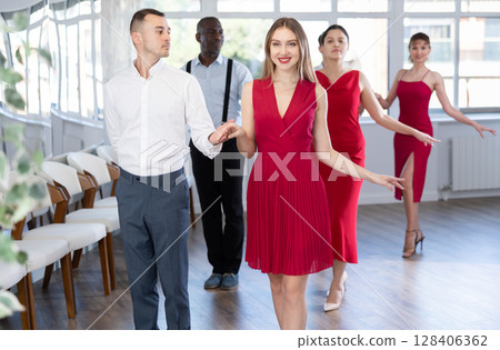 Beautiful girls dressed in red dress dancing waltz with partners in dancing class during multinational group party 128406362