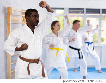 Multinational students repeat position and perform sequence of punches and painful techniques kata 128406433