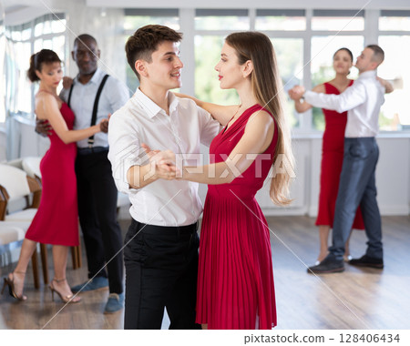Young guy and woman in red dress waltzing during group class Young guy and woman in red dress waltzing during group class 128406434