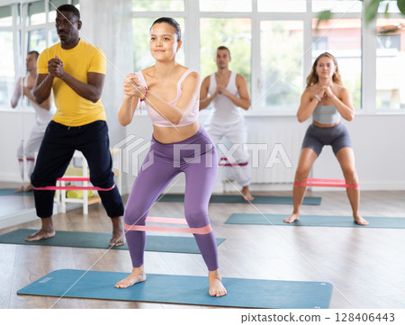 Asian woman exercising with loop band during group pilates class Asian woman exercising with loop band during group pilates class 128406443