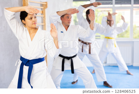 Middle-aged woman attendee of karate classes practicing kata standing in row with others 128406525