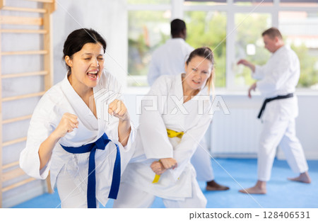 Middle-aged woman attendee of karate classes fighting with her opponent in sports hall Middle-aged woman attendee of karate classes fighting with her opponent in sports hall 128406531
