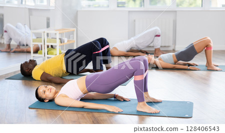 Asian woman exercising with loop band during group pilates class Asian woman exercising with loop band during group pilates class 128406543