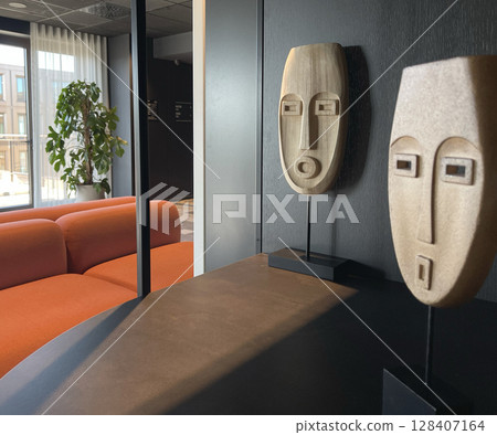 Wooden mask on stand in room. Design in interior. Simple art object in room on dark background. Wooden mask on stand in room. Design in interior. Simple art object in room on dark background. 128407164