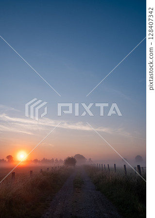 A Beautiful and Serene Sunrise Over the Misty Countryside Path Invites Exploration and Adventure A Beautiful and Serene Sunrise Over the Misty Countryside Path Invites Exploration and Adventure 128407342