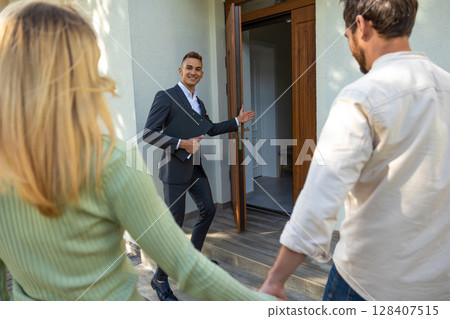 Realtor guiding couple inside modern residence with open door 128407515