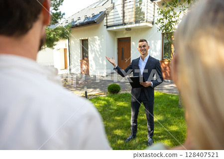 Agent showing new home to clients in suburban garden setting 128407521