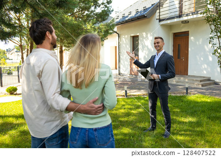 Real estate agent presenting modern house to couple in sunny yard 128407522