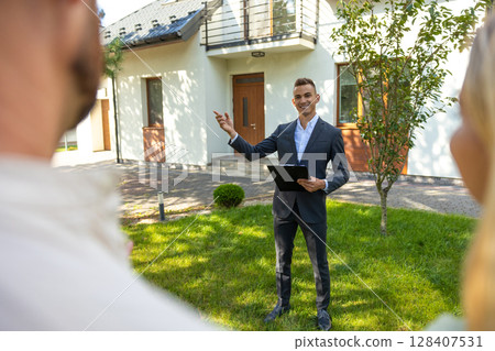 Real estate agent presenting modern house to couple in sunny yard Real estate agent presenting modern house to couple in sunny yard 128407531