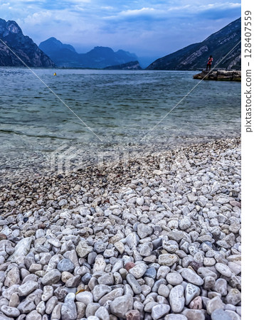 Rocky shore of Lake Garda with clear water and mountains under cloudy sky. High quality photo Rocky shore of Lake Garda with clear water and mountains under cloudy sky. High quality photo 128407559
